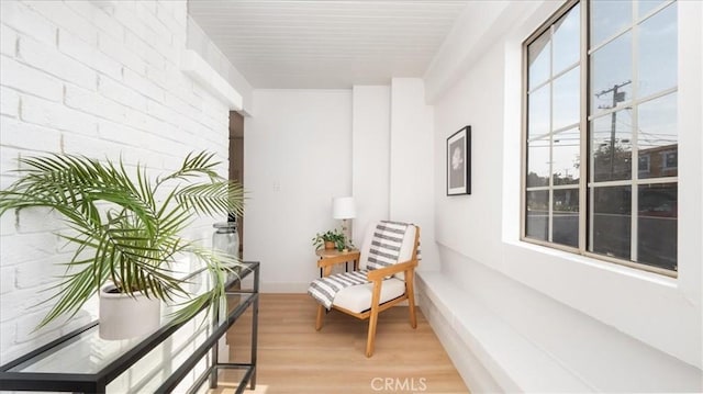 sitting room featuring light wood finished floors, baseboards, and brick wall