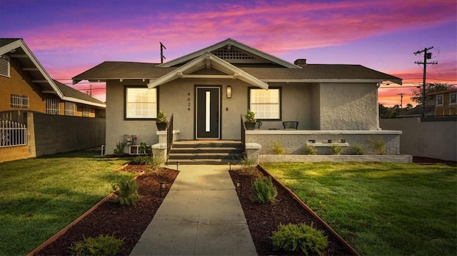 bungalow-style house with stucco siding, fence, and a yard