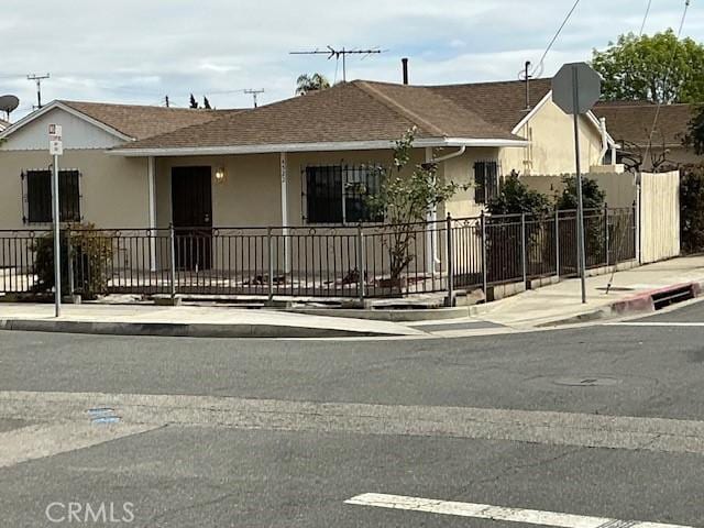 view of front of house with roof with shingles, stucco siding, and fence