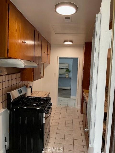 4522 W 156th St, Lawndale, CA 90260 - kitchen with stainless steel gas range oven, under cabinet range hood, light tile patterned floors, light countertops, and brown cabinets