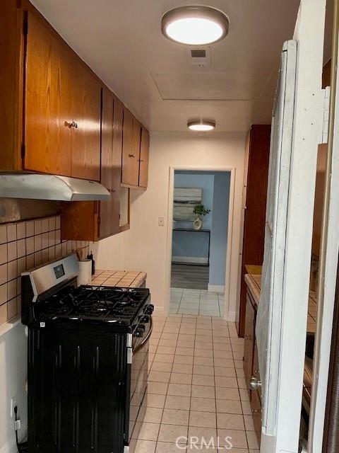 4522 W 156th St, Lawndale, CA 90260 - kitchen with stainless steel range with gas cooktop, under cabinet range hood, light tile patterned floors, and brown cabinets