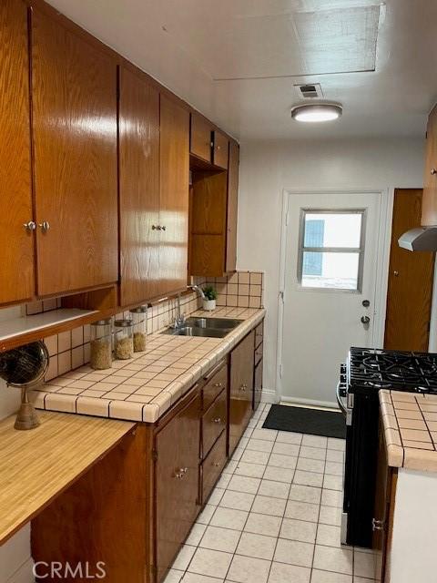 kitchen with tasteful backsplash, a sink, black gas range oven, tile countertops, and light tile patterned flooring