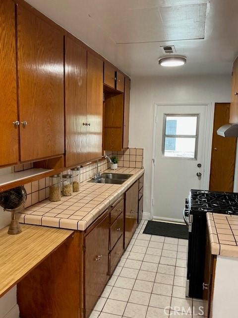 4522 W 156th St, Lawndale, CA 90260 - kitchen with range with gas cooktop, tile counters, a sink, light tile patterned floors, and tasteful backsplash