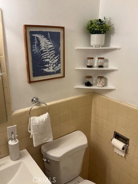 bathroom featuring toilet, a wainscoted wall, and tile walls