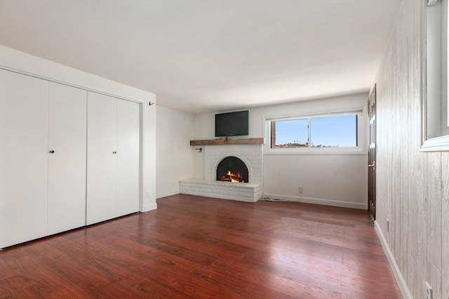 unfurnished living room with baseboards, wood finished floors, and a brick fireplace