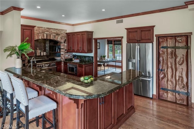 kitchen featuring wood finished floors, dark stone counters, stainless steel appliances, visible vents, and a peninsula