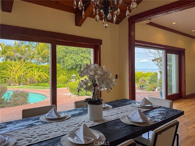 dining space with beamed ceiling, light wood finished floors, and an inviting chandelier