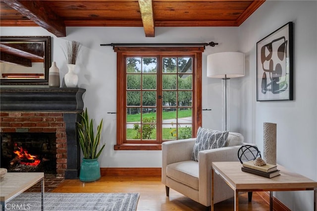 sitting room featuring wooden ceiling, beam ceiling, a fireplace, baseboards, and wood finished floors