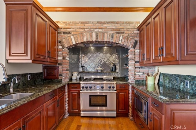 kitchen featuring dark stone countertops, tasteful backsplash, stainless steel appliances, light wood finished floors, and a sink