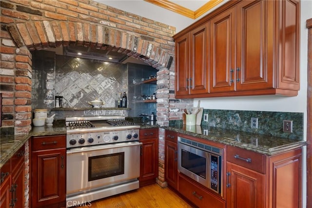 kitchen with ornamental molding, dark stone countertops, backsplash, and stainless steel appliances