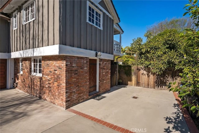 view of side of property featuring fence, board and batten siding, a patio, and brick siding