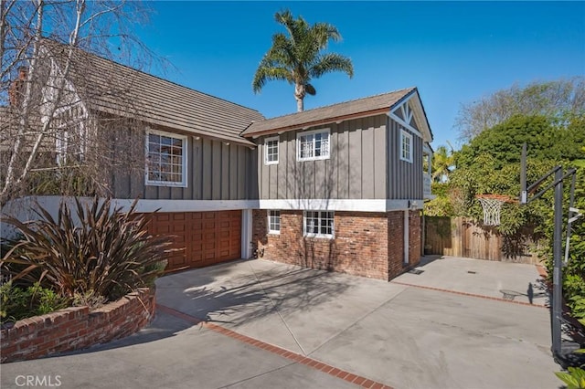 exterior space with concrete driveway, fence, board and batten siding, and brick siding