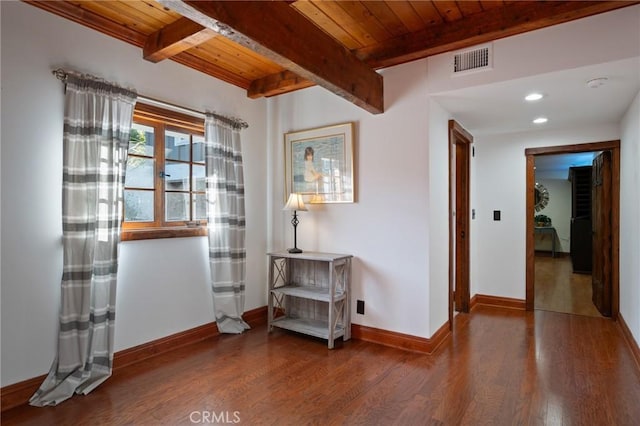 empty room with wood finished floors, wood ceiling, beamed ceiling, baseboards, and visible vents