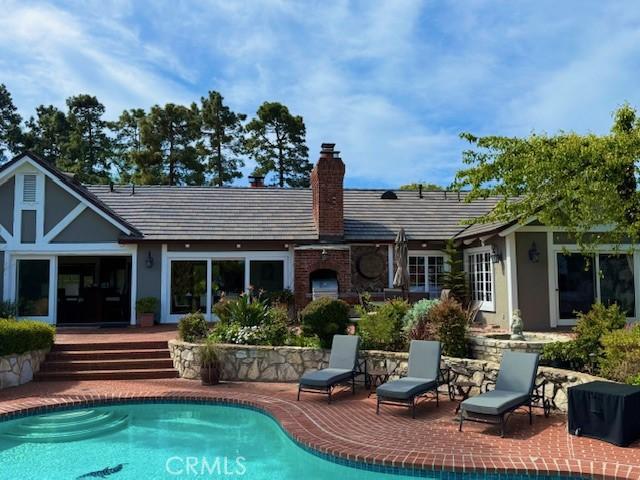back of house featuring an outdoor pool, stucco siding, a patio area, and a chimney