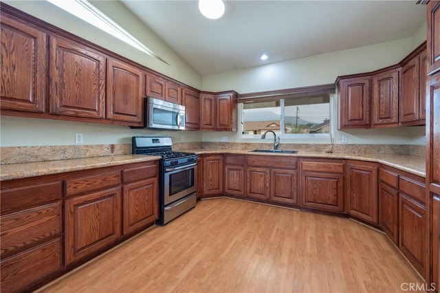 kitchen with light stone countertops, light wood-style floors, brown cabinetry, appliances with stainless steel finishes, and a sink