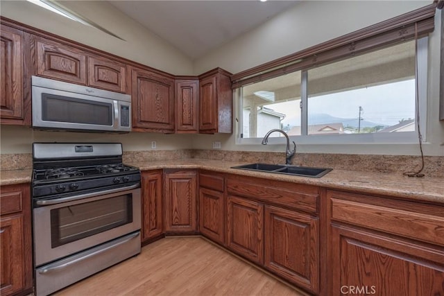 kitchen featuring brown cabinetry, light countertops, a sink, stainless steel appliances, and light wood finished floors