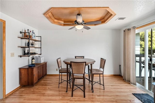 dining space featuring a raised ceiling, a ceiling fan, a textured ceiling, light wood-type flooring, and visible vents