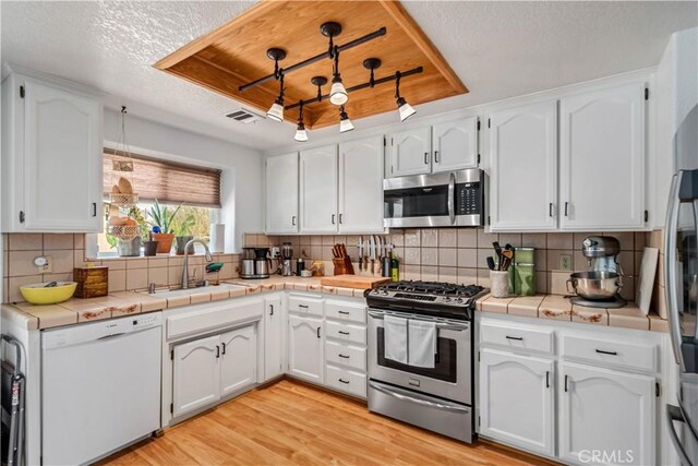 kitchen with a tray ceiling, white cabinets, a sink, and stainless steel appliances