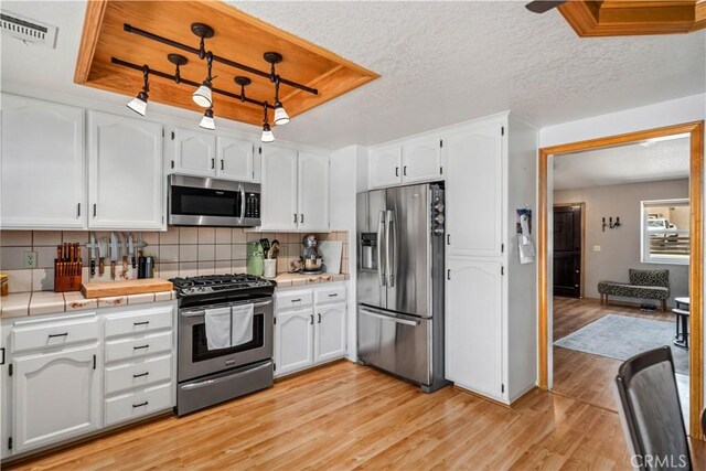 kitchen with white cabinetry, stainless steel appliances, tile countertops, and visible vents