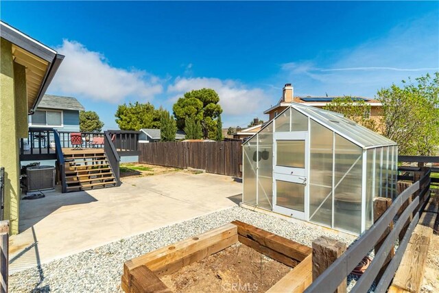 view of patio with central air condition unit, a wooden deck, a greenhouse, a fenced backyard, and an outdoor structure