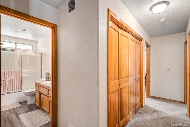 hall featuring a textured ceiling, visible vents, baseboards, light carpet, and a textured wall