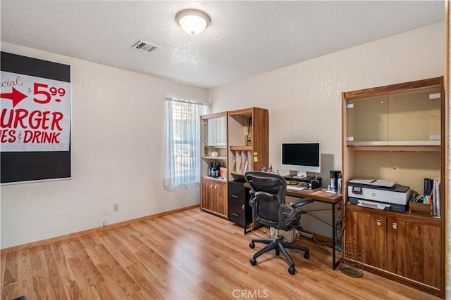 home office featuring a textured ceiling, baseboards, light wood-style flooring, and visible vents
