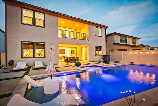 back of house with a hot tub, a patio area, central AC, a balcony, and stucco siding