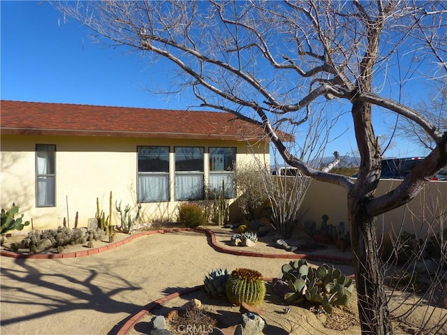back of house featuring stucco siding, a shingled roof, and fence