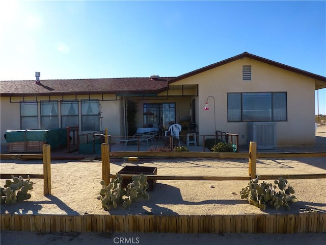 back of property with stucco siding, cooling unit, roof with shingles, and a patio area