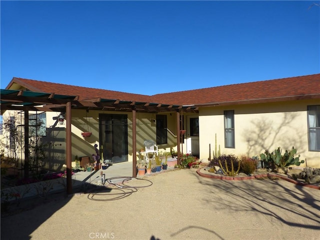 back of house with stucco siding, a shingled roof, and a patio area