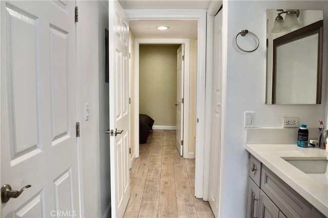 hall featuring baseboards, recessed lighting, light wood-style floors, and a sink