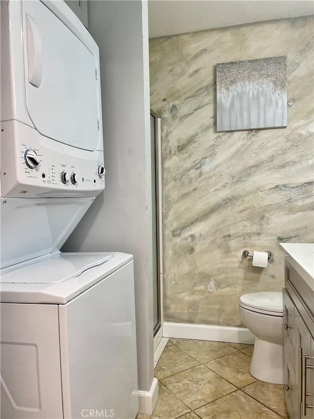 washroom featuring light tile patterned floors, stacked washer and dryer, baseboards, and laundry area