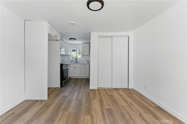 unfurnished bedroom featuring a sink, baseboards, light wood-style floors, and a closet