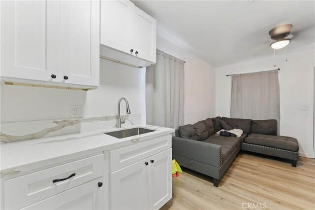 kitchen with white cabinetry, a sink, light wood-style floors, and light stone countertops
