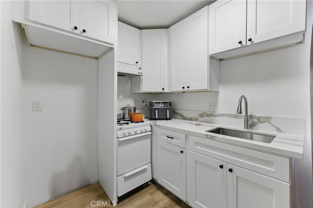 kitchen featuring gas range gas stove, under cabinet range hood, a sink, light wood-style floors, and white cabinets