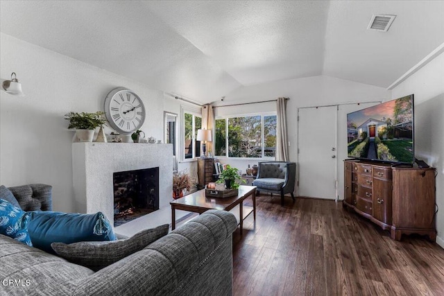 living room featuring lofted ceiling, a textured ceiling, visible vents, a fireplace, and wood finished floors