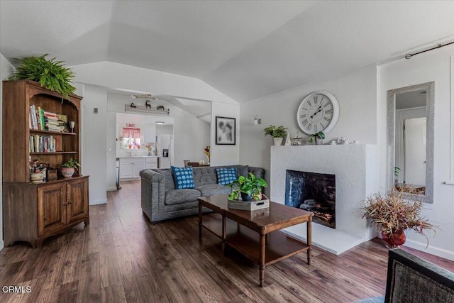 living area with a fireplace with raised hearth, vaulted ceiling, and wood finished floors