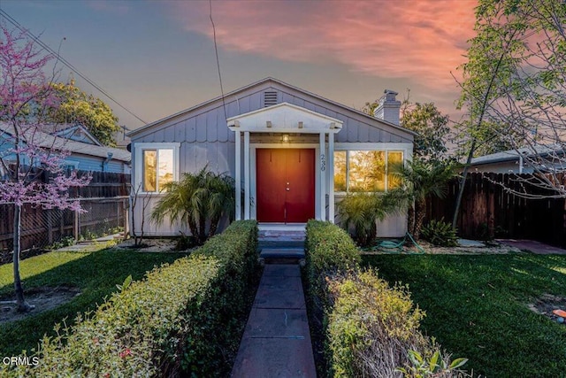 view of front of house featuring a chimney, fence, and a front lawn