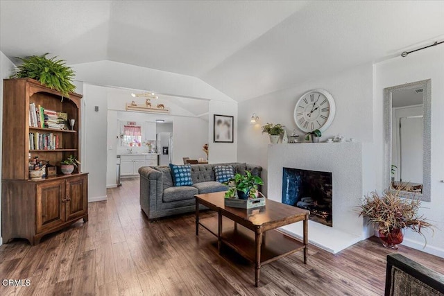 living area with lofted ceiling, wood finished floors, and a fireplace with raised hearth