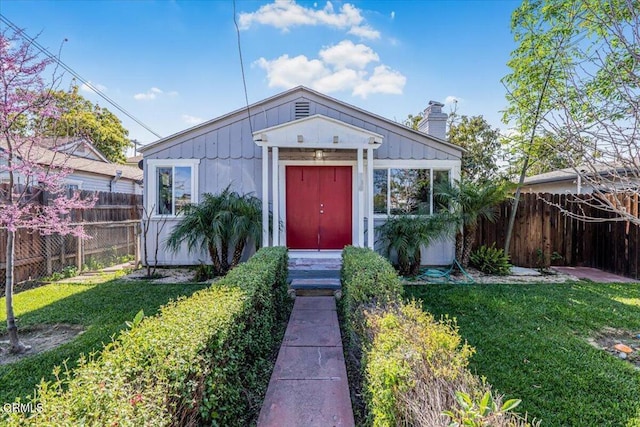 bungalow-style house featuring a front yard, fence, and a chimney