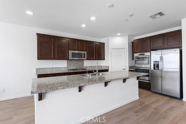 kitchen with a sink, a breakfast bar area, stainless steel appliances, visible vents, and light wood-style floors