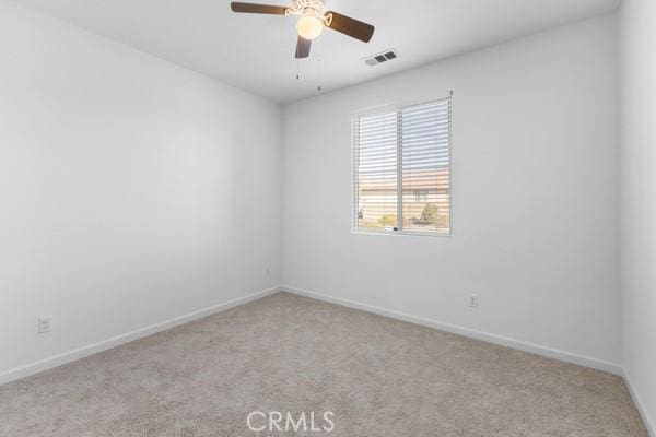 carpeted empty room featuring baseboards, visible vents, and a ceiling fan