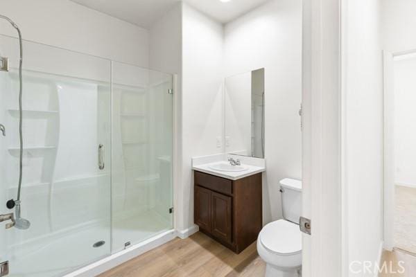 bathroom with wood finished floors, a stall shower, toilet, and vanity