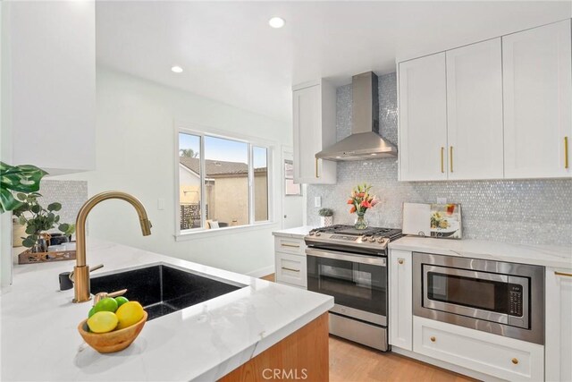 2902 Ladoga Ave, Long Beach, CA 90815 - kitchen featuring wall chimney range hood, stainless steel appliances, a sink, white cabinets, and backsplash