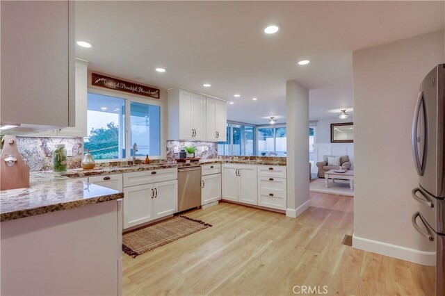 kitchen with white cabinets, appliances with stainless steel finishes, decorative backsplash, and light stone countertops