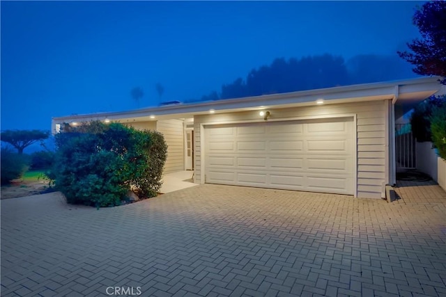garage at twilight featuring decorative driveway