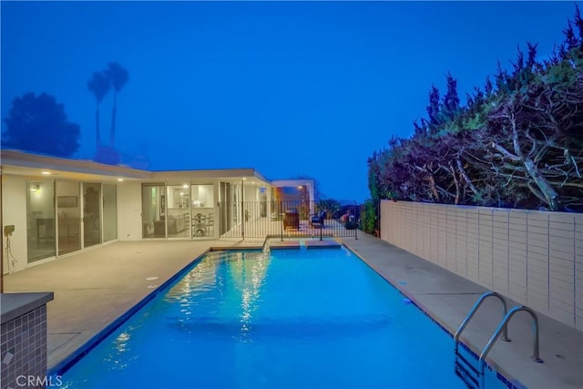 pool at night featuring a patio area, fence, and a fenced in pool