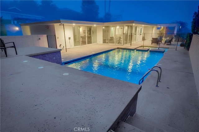 pool at night featuring fence, a patio, and a fenced in pool