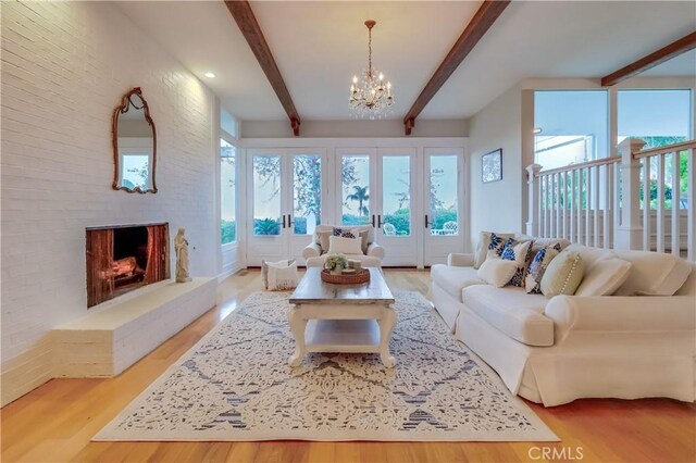living room with beam ceiling, a fireplace, brick wall, light wood-type flooring, and a chandelier