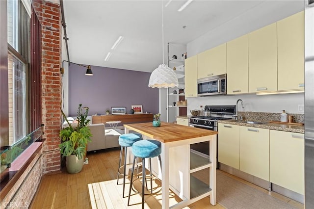 460 S Spring St Unit 302, Los Angeles, CA 90013 - kitchen with light wood finished floors, gas range oven, cream cabinetry, stainless steel microwave, and butcher block countertops